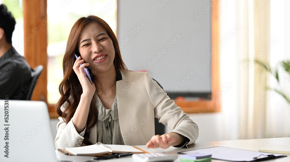 Obraz premium Friendly female financial advisor consulting client on cellphone and using laptop computer at corporate office