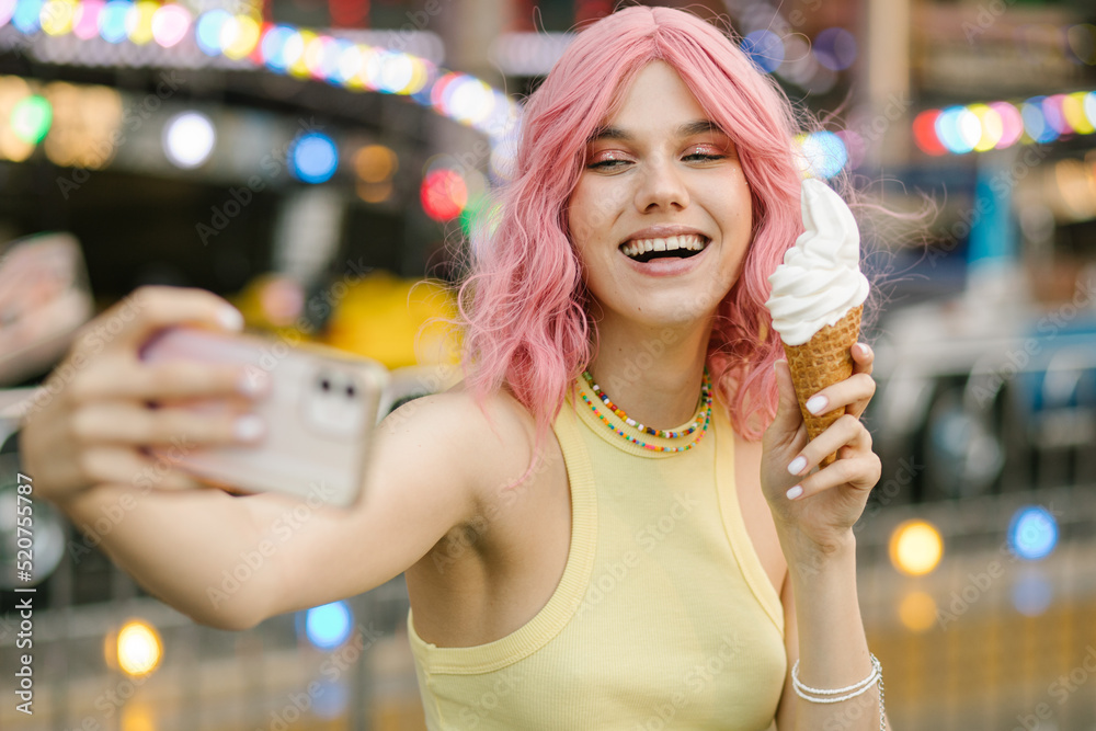 Cute girl eating ice cream. A girl with pink hair poses with ice cream. Stylish girl in a yellow top. Attractions on the background Cute girl eating ice cream. A girl with pink hair poses with ice cream. Stylish girl in a yellow top. Attractions on the background