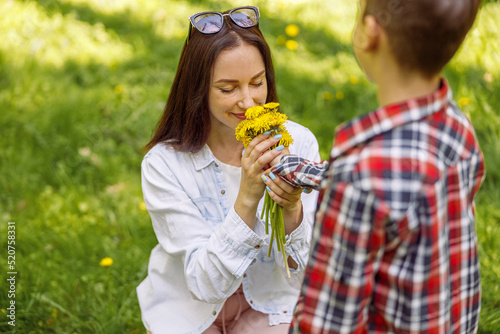 Cheerful happy mother having dandelions as present from son. Boy presenting flowers to woman. 