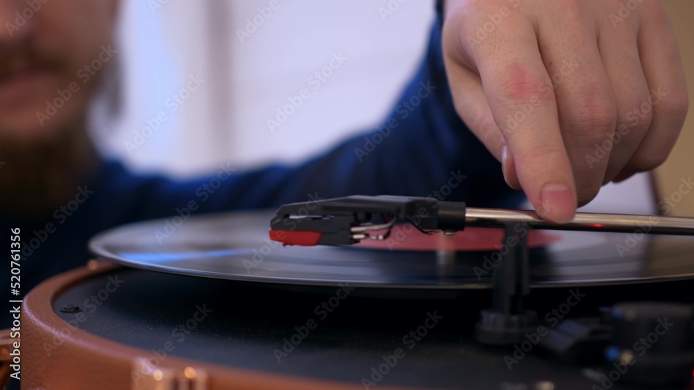 Close-up of a man putting a vinyl record into a turntable, the record starts spinning and a needle is slowly lowered onto it to play music. Vintage listening to music at home. Close-up of a man putting a vinyl record into a turntable, the record starts spinning and a needle is slowly lowered onto it to play music. Vintage listening to music at home.