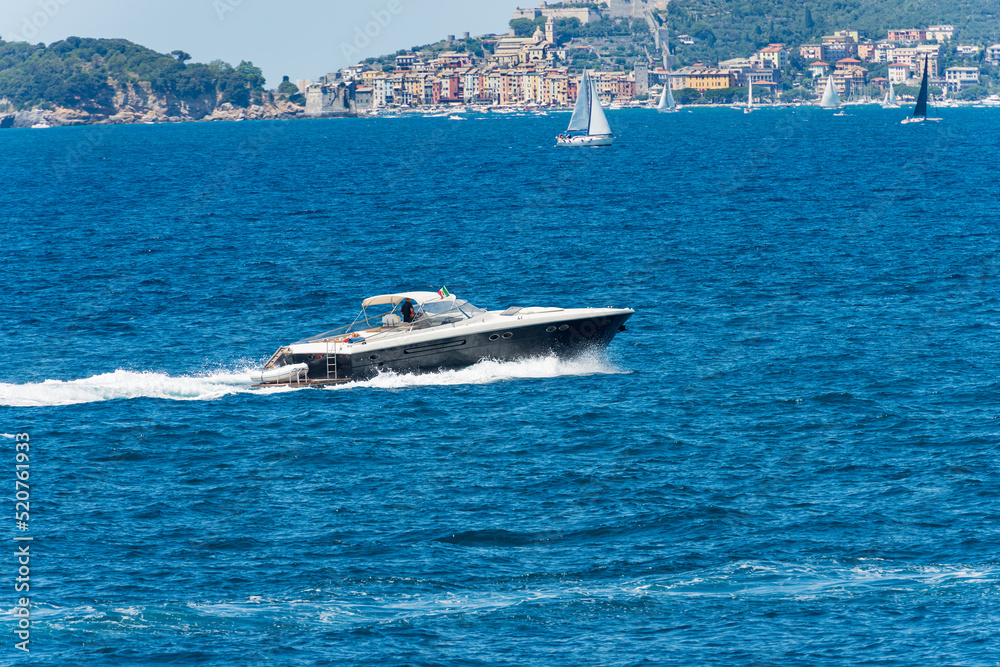 Fototapeta premium Blue and white luxury speedboat or yacht in motion on Mediterranean sea in front of the Porto Venere or Portovenere, Gulf of La Spezia, UNESCO world heritage site, La Spezia, Liguria, Italy, Europe.