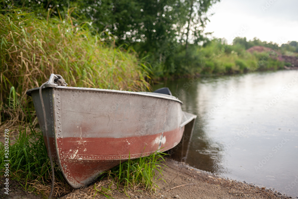 A motor boat is parked at the shore of a lake or river in the evening at sunset or early in the morning. The boat is in a quiet place next to the reeds and is ready for fishing. A motor boat is parked at the shore of a lake or river in the evening at sunset or early in the morning. The boat is in a quiet place next to the reeds and is ready for fishing.