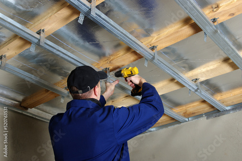 Builder installs profile metal frame for plasterboard ceilings