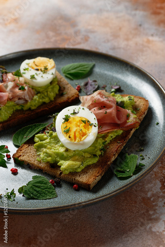 Toasted slice of bread topped with avocado, a hard-boiled egg and ham. Healthy toast (tartine).
