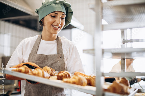 Female baker at the kitchen holding freshly baked croiisants photo