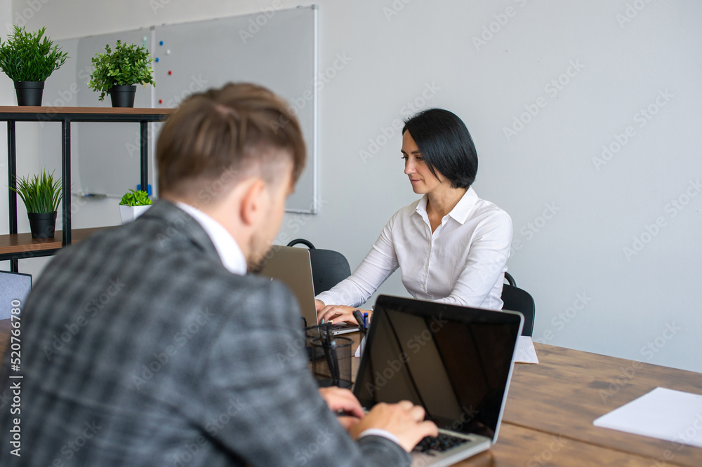 Work in an office, a woman sits opposite a man, typing text Work in an office, a woman sits opposite a man, typing text