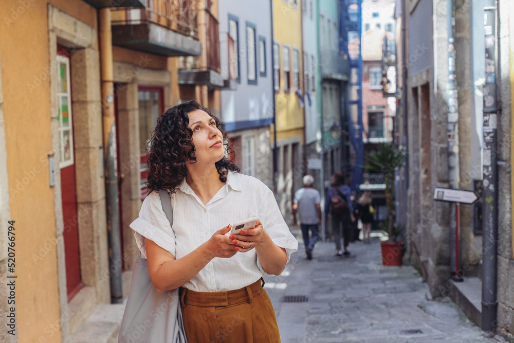 Lost woman in casual clothes walking on an old European street, looking around, using a map on her smartphone Lost woman in casual clothes walking on an old European street, looking around, using a map on her smartphone
