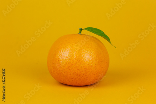 An Orange fruit with green leaf isolated on yellow background. One orange fruit with leaf stand on isolating concept for ads design