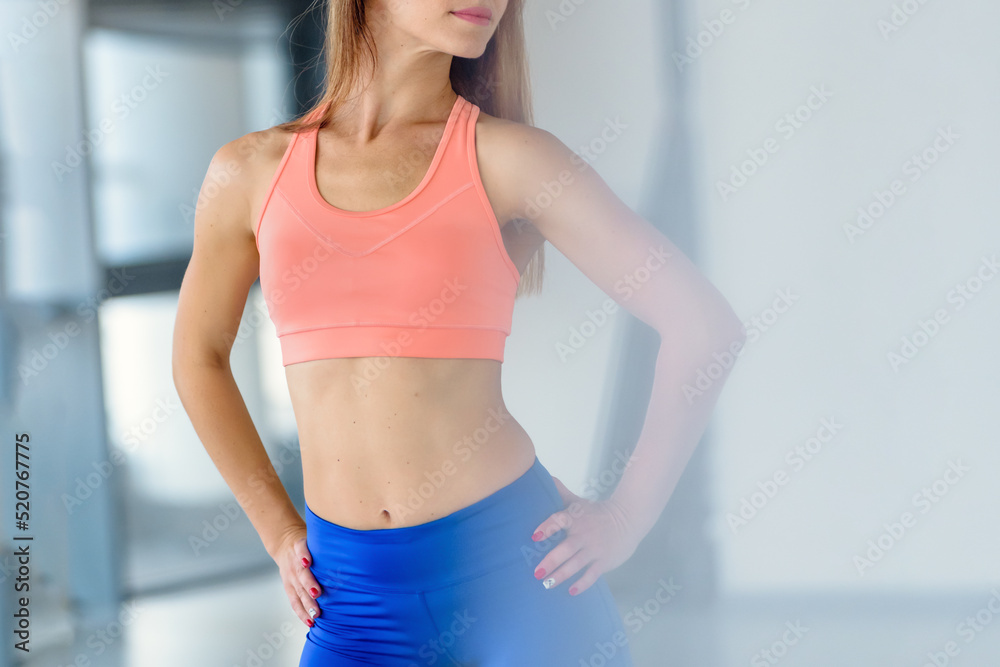 Beautiful young sporty woman with perfect body doing stretching exercise in gym