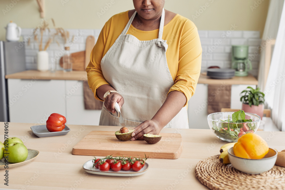 Cropped portrait of black woman cutting avocado while cooking healthy meal in kitchen, copy space - obrazy, fototapety, plakaty 