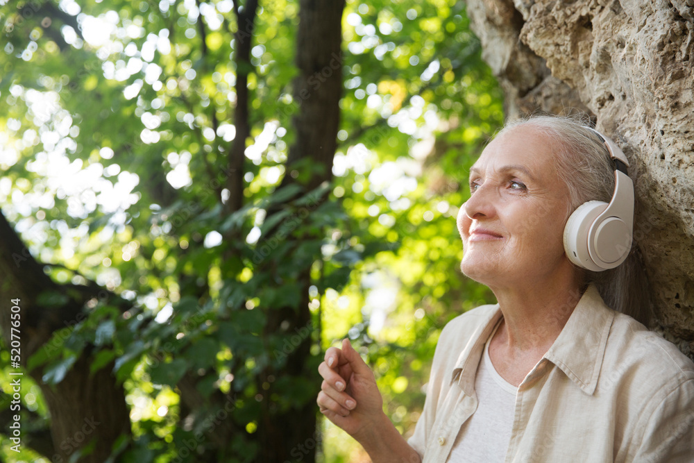 Summer lifestyle portrait senior woman in headphones relax on the outdoor. Enjoying the little things. spends time in nature in summer. Audio healing. meditation. Summer lifestyle portrait senior woman in headphones relax on the outdoor. Enjoying the little things. spends time in nature in summer. Audio healing. meditation.