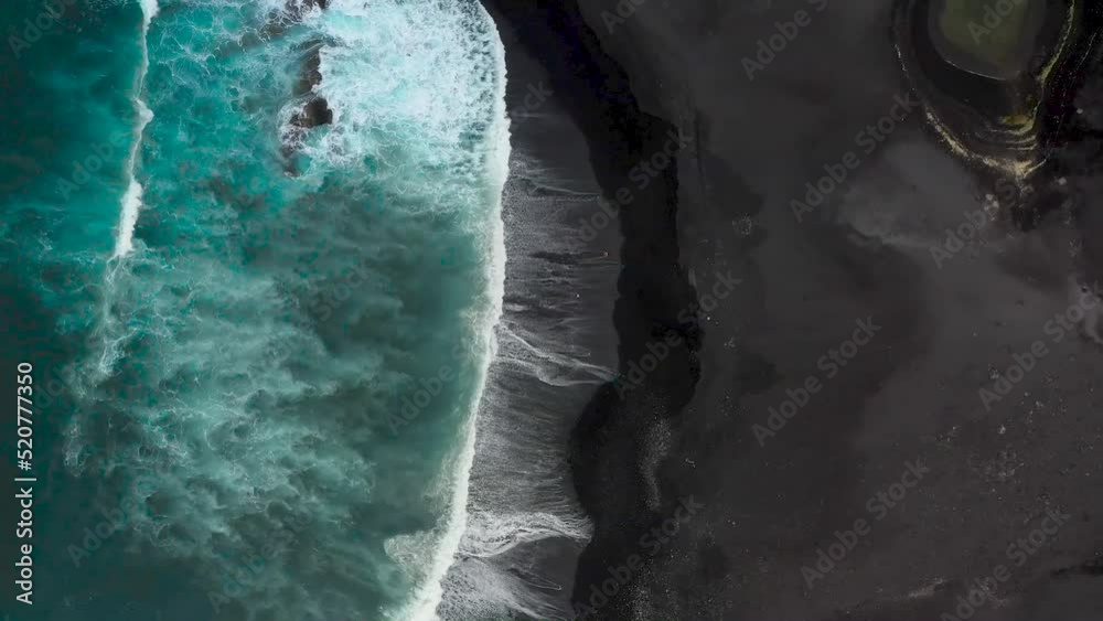 Blaues Meer und schwarzer Strand mit der Drohne gefilmt. Ein Pärchen läuft am schwarzen Strand entlang. Vogelperspektive am Strand. 2