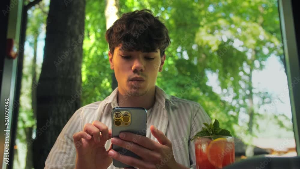 Surprised Young man using phone sitting in restaurant.Smiling man holding phone and online shopping Surprised Young man using phone sitting in restaurant.Smiling man holding phone and online shopping