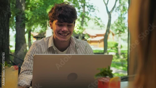 Young man using laptop sitting in restaurant.Businessman Works remotely in the background of panoramic windows.Smiling man againgst green trees.Couple relaxing in cafe photo