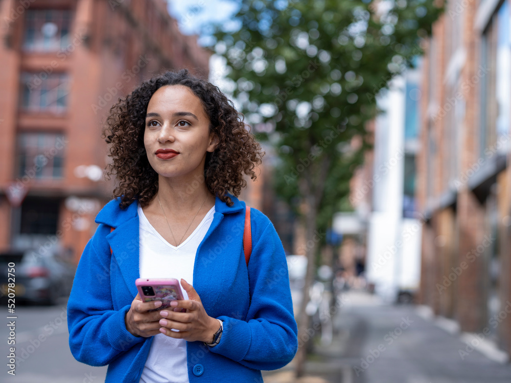 UK, Smiling woman holding smart phone on street UK, Smiling woman holding smart phone on street