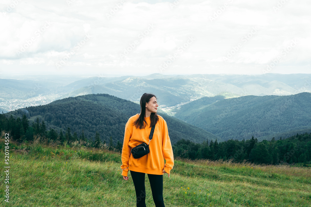 Photo of a tourist woman in casual clothes posing for the camera in the mountains against the background of Carpathian views, looking away with a serious face. Photo of a tourist woman in casual clothes posing for the camera in the mountains against the background of Carpathian views, looking away with a serious face.