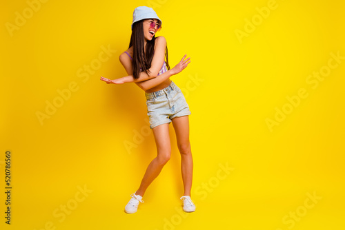 Full length photo of funky charming girl dressed swimsuit bra cap dark eyewear dancing empty space isolated yellow color background © deagreez