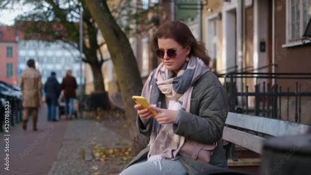 Traveller european woman have a chat in smartphone sitting on the bench in the street of old town, 4k 60p Traveller european woman have a chat in smartphone sitting on the bench in the street of old town, 4k 60p