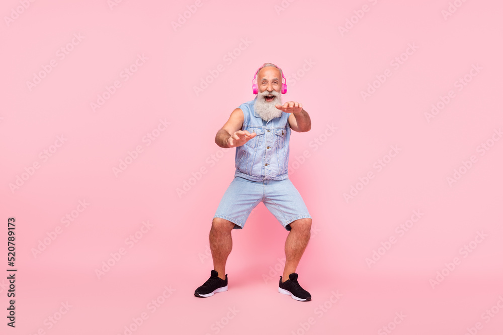Full length photo of charming cool retired guy wear jeans waistcoat earphones having fun isolated pink color background Full length photo of charming cool retired guy wear jeans waistcoat earphones having fun isolated pink color background