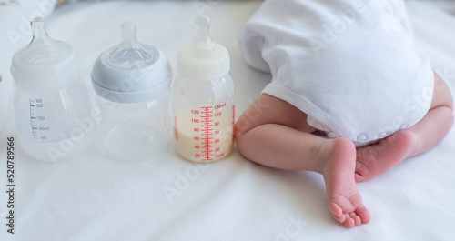 Baby s little butt with bend up legs and three bottles for milk on white blanket. Newborn - happiness for family. Concept of choice milk formula and food for kid. Back view