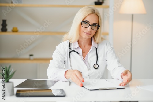 Portrait shot of middle aged female doctor sitting at desk and working in doctor office