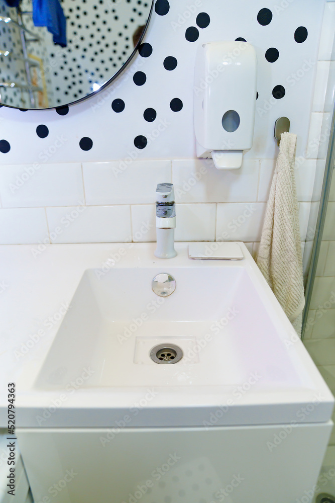 Fototapeta premium a white washbasin in the bathroom with a mirror and a soap dispenser on the wall