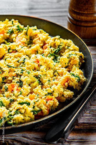 scrambled eggs with spinach and tomato in pan on wooden table background