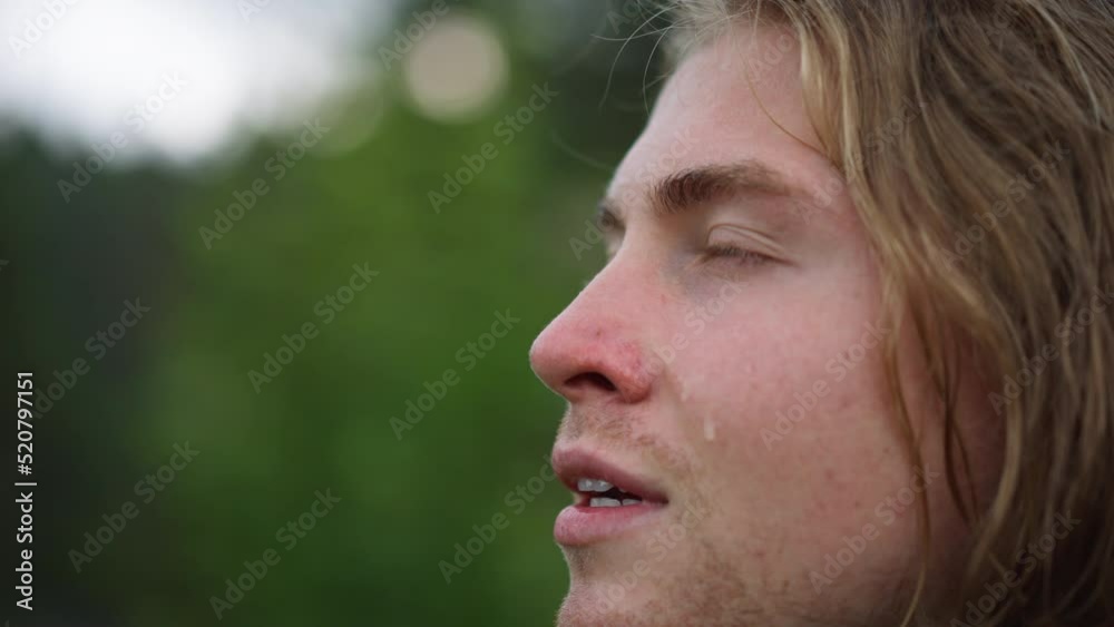 Young carefree handsome young man is feeling free under the rain on a background of green trees.