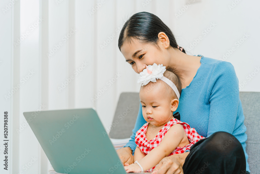 Young Asian mom with cute baby daughter sitting at sofa together in the living room. Young Asian mom with cute baby daughter sitting at sofa together in the living room.