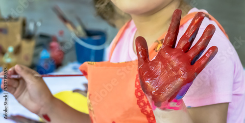 Close up young kid artist with dirty hands in art school, playful messy girl artist showing red colored hand  photo