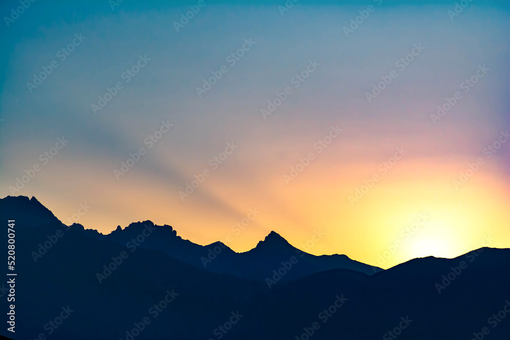 Beautiful fiery sunset and high mountains. The sun goes behind the mountains. Beautiful nature