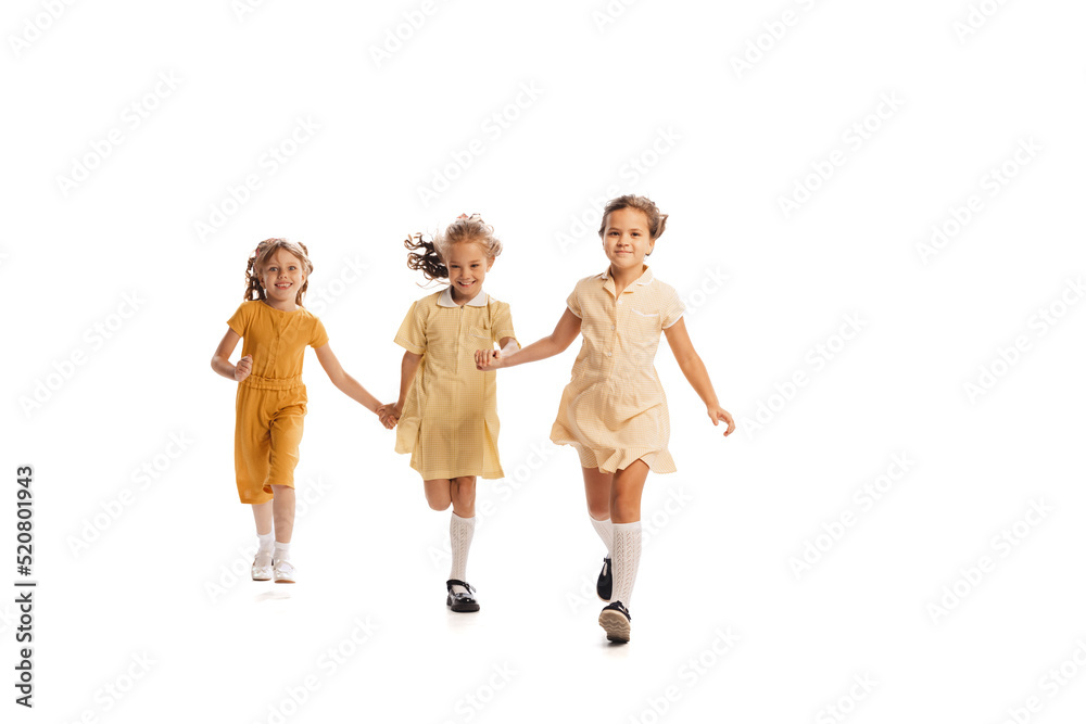 Portrait of three little girls in yellow stylish dresses playing together isolated over white studio background. Cheerfully running Portrait of three little girls in yellow stylish dresses playing together isolated over white studio background. Cheerfully running