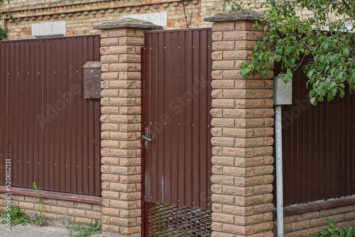 one closed iron brown door and part of a wall fence made of bricks and metal on a rural street © butus