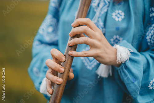 Woman playing woodwind wooden flute - ukrainian sopilka outdoors. Folk music, culture concept. Musical instrument. Lady in traditional embroidered shirt - blue vyshyvanka.