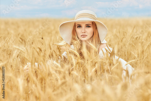 Blonde girl in a wheat field in a white dress and a straw hat in summer