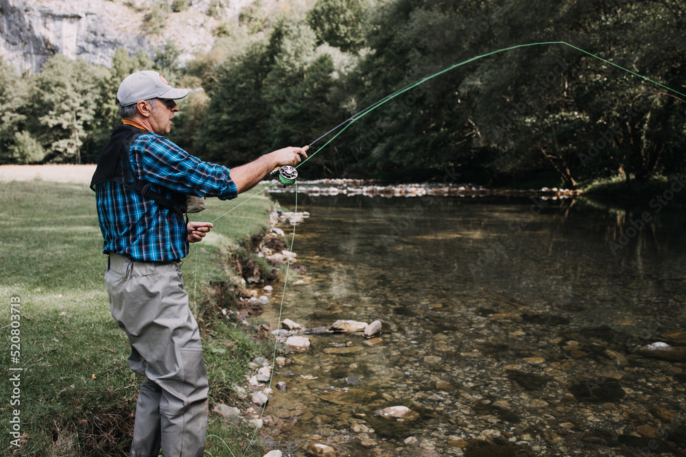 Senior man is fishing alone on fast mountain river. Active people and sport fly fishing concept. Senior man is fishing alone on fast mountain river. Active people and sport fly fishing concept.