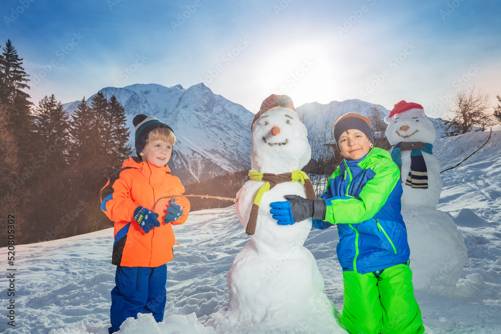 Two happy smiling kids build and dress snowman outside