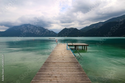 Attersee - famous Austrian turquoise lake. The view on the long wooden pier and the mountains in the background. Cloudy sky. 