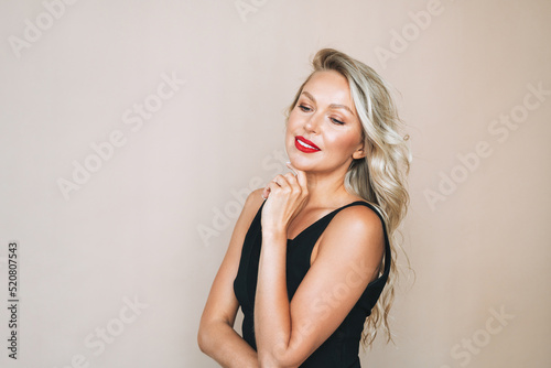 Portrait of gorgeous beautiful blonde young woman with bright makeup in evening dress on beige background