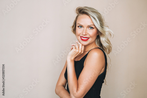 Portrait of gorgeous beautiful blonde young woman with bright makeup in evening dress on beige background