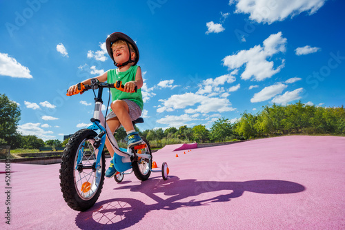 Small boy learn to ride bicycle with learning wheels, low angle
