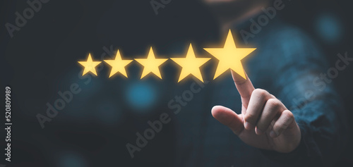Businessman touching glowing yellow five stars for excellent evaluate after customer use product service , ISO and quality standard certificate concept. photo