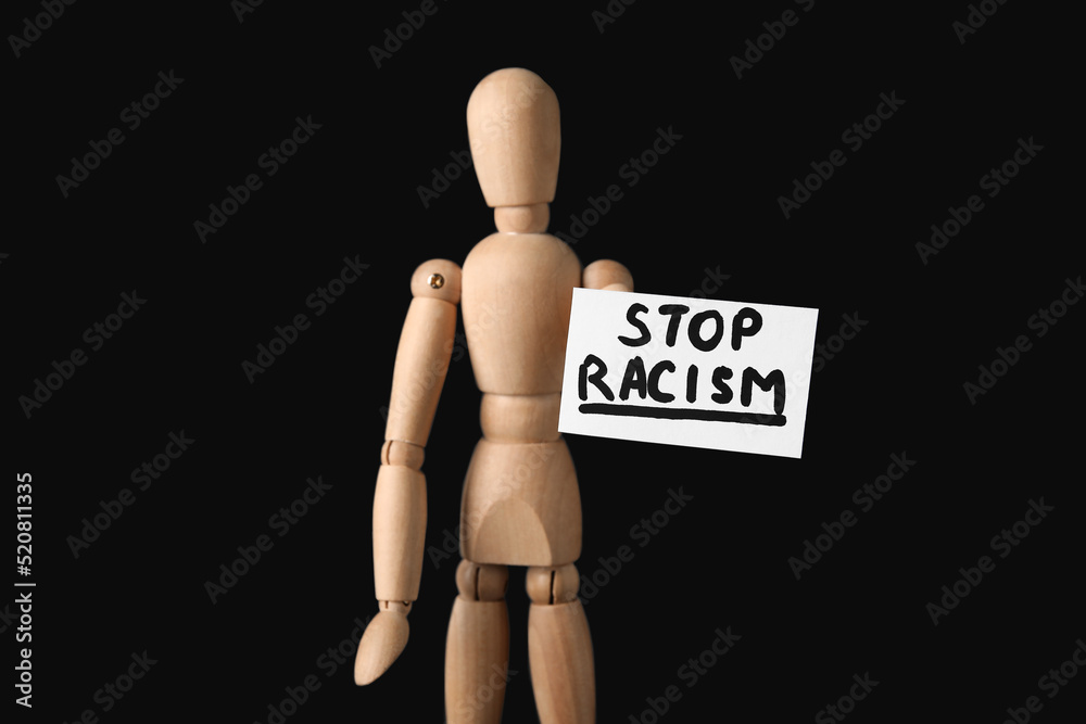 Wooden mannequin and paper sheet with text STOP RACISM on dark background Wooden mannequin and paper sheet with text STOP RACISM on dark background