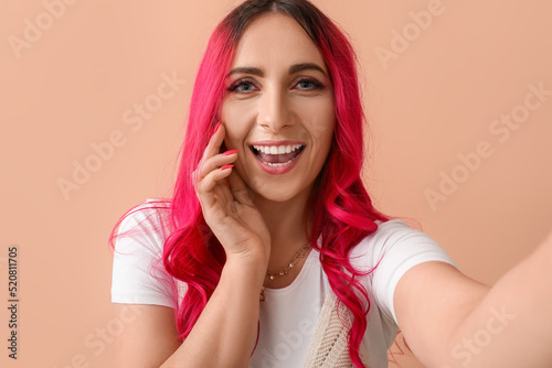 Beautiful woman with bright pink hair taking selfie on beige background