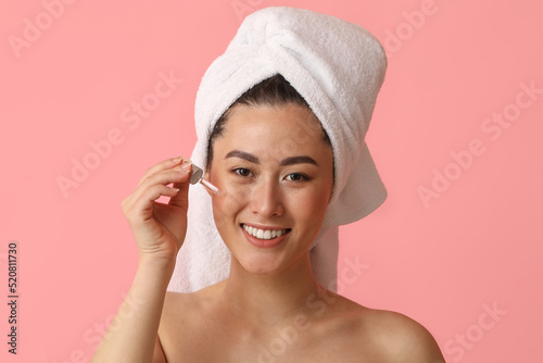 Young Asian woman with cosmetic serum on pink background