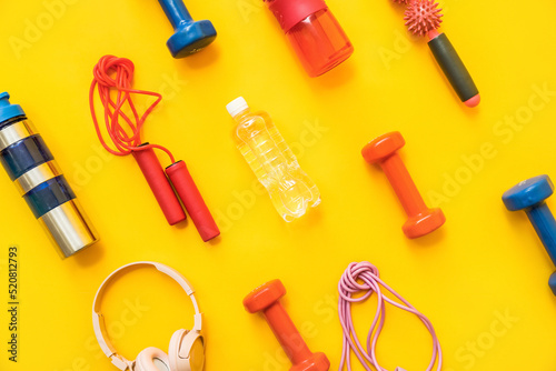 Different sports equipment, bottle of water and headphones on yellow background