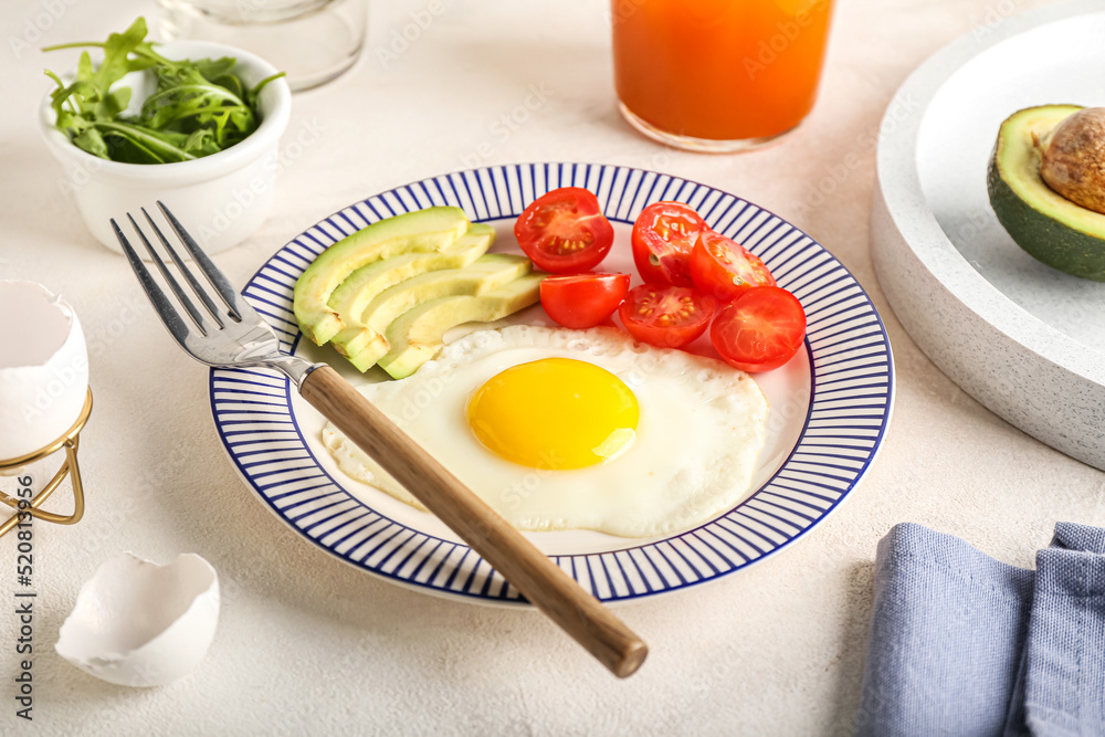 Plate with tasty fried egg, tomatoes and avocado on light table Plate with tasty fried egg, tomatoes and avocado on light table