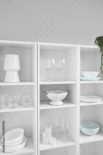 Big shelving unit with tableware near light wall