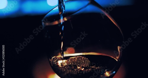 Close-up of Female hand holding and fill wine in a glass on defocused cozy camp fire of background 