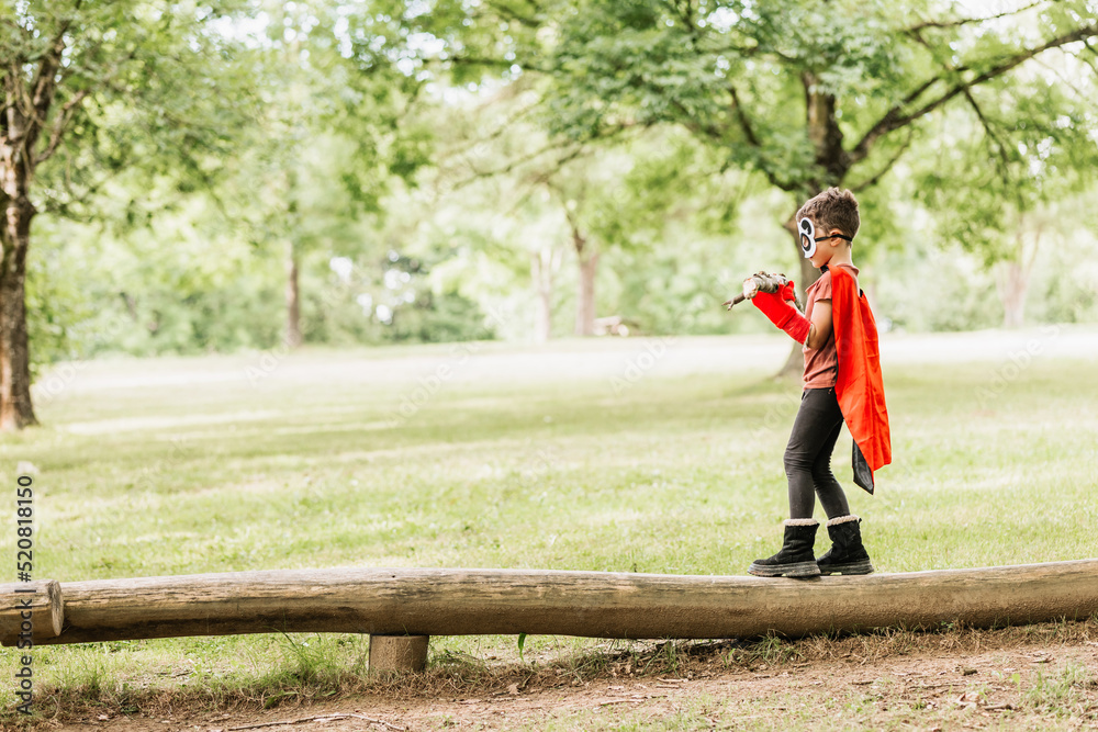 Boy in superhero costume balancing on log Boy in superhero costume balancing on log
